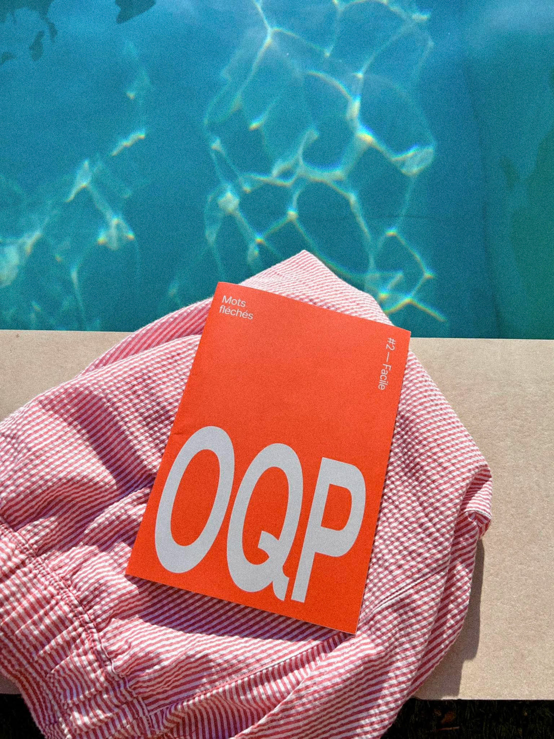 Le livret OQP #2 posé sur une serviette au bord de la piscine